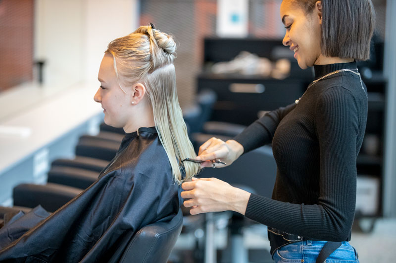 Female apprentice cuts hair on customer. Photo.